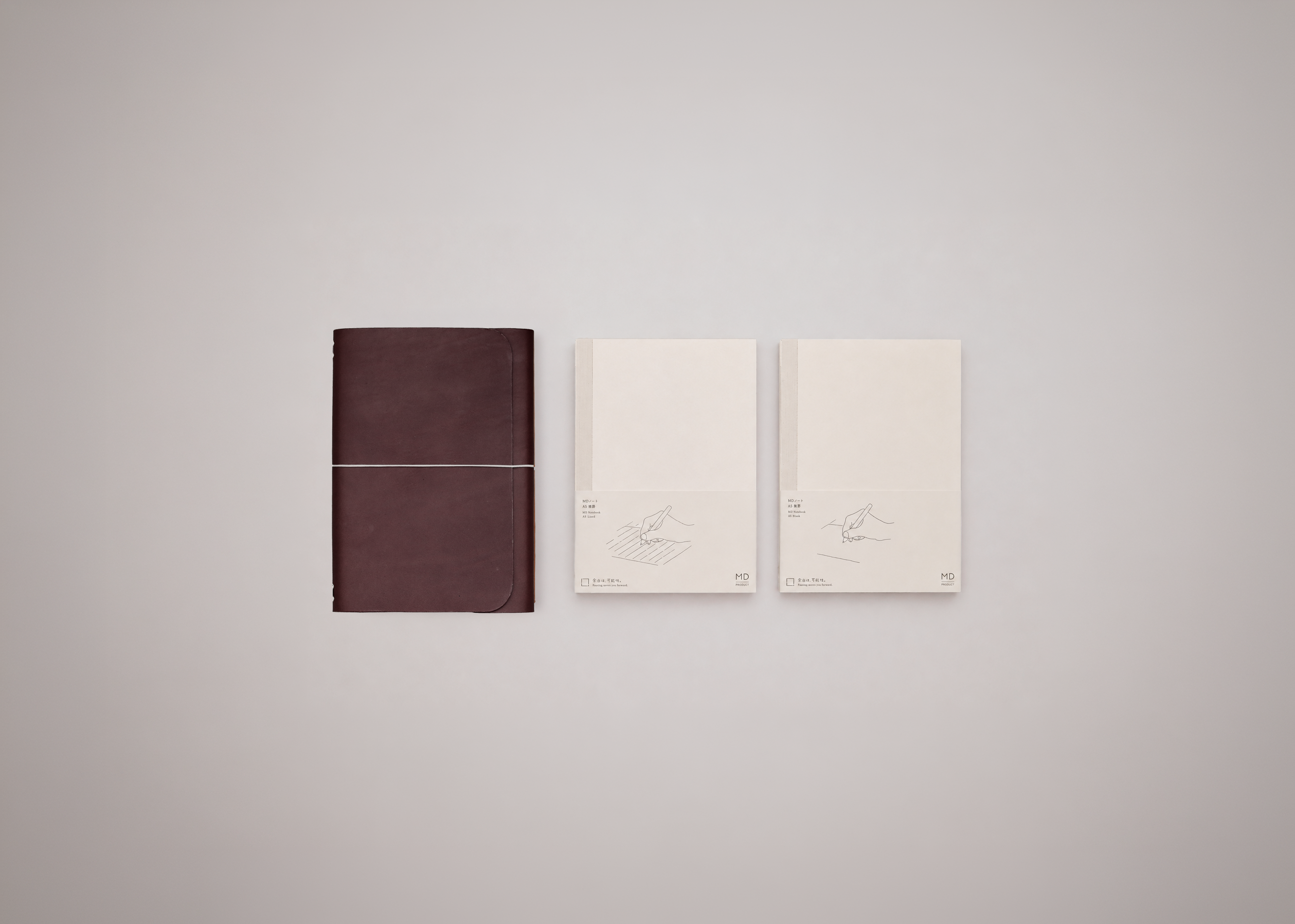 One leather journal cover in dark brown next to two white notebook inserts against a light grey background