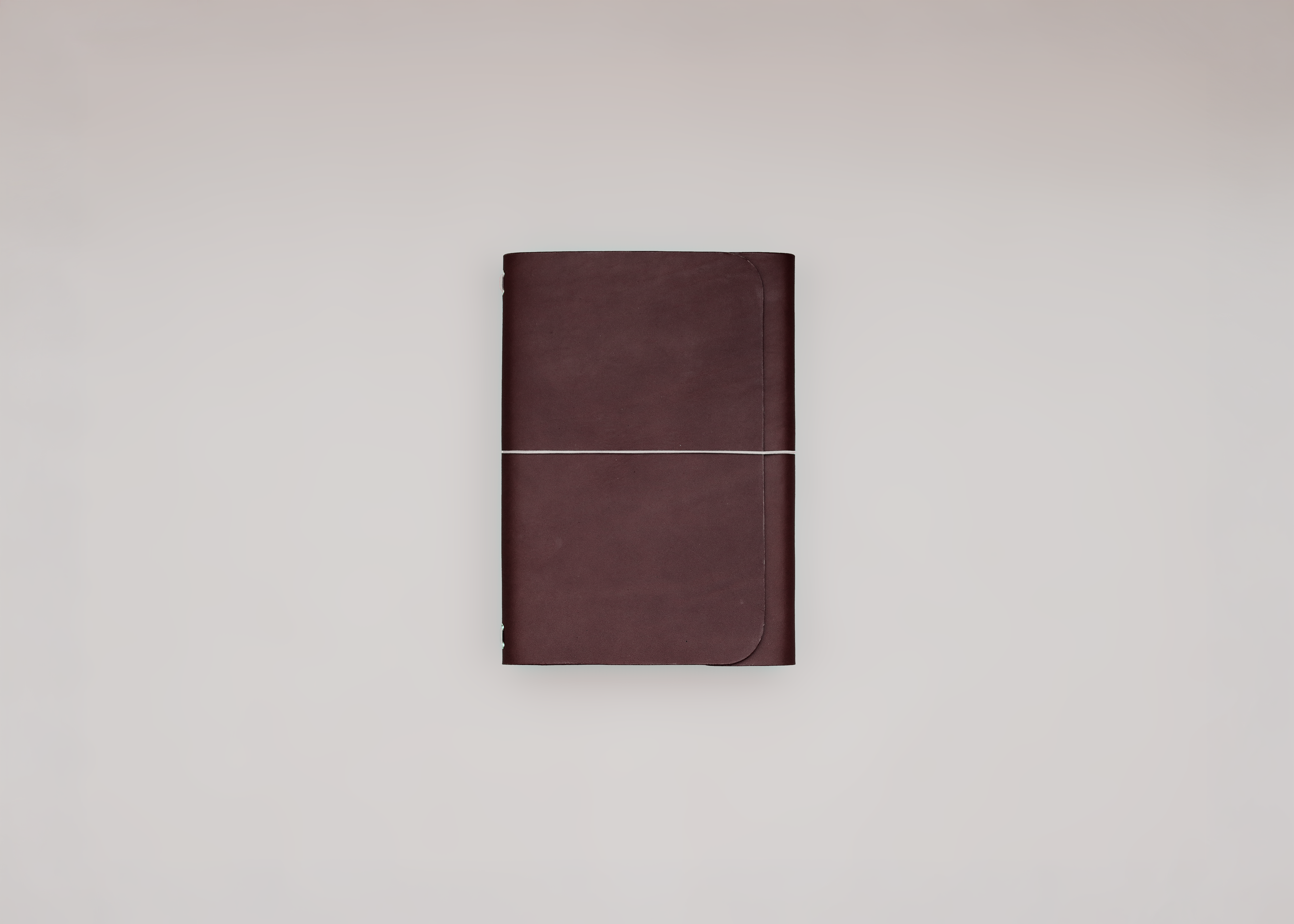 A dark brown leather journal with a horizontal elastic closure band, centered against a plain light grey background.