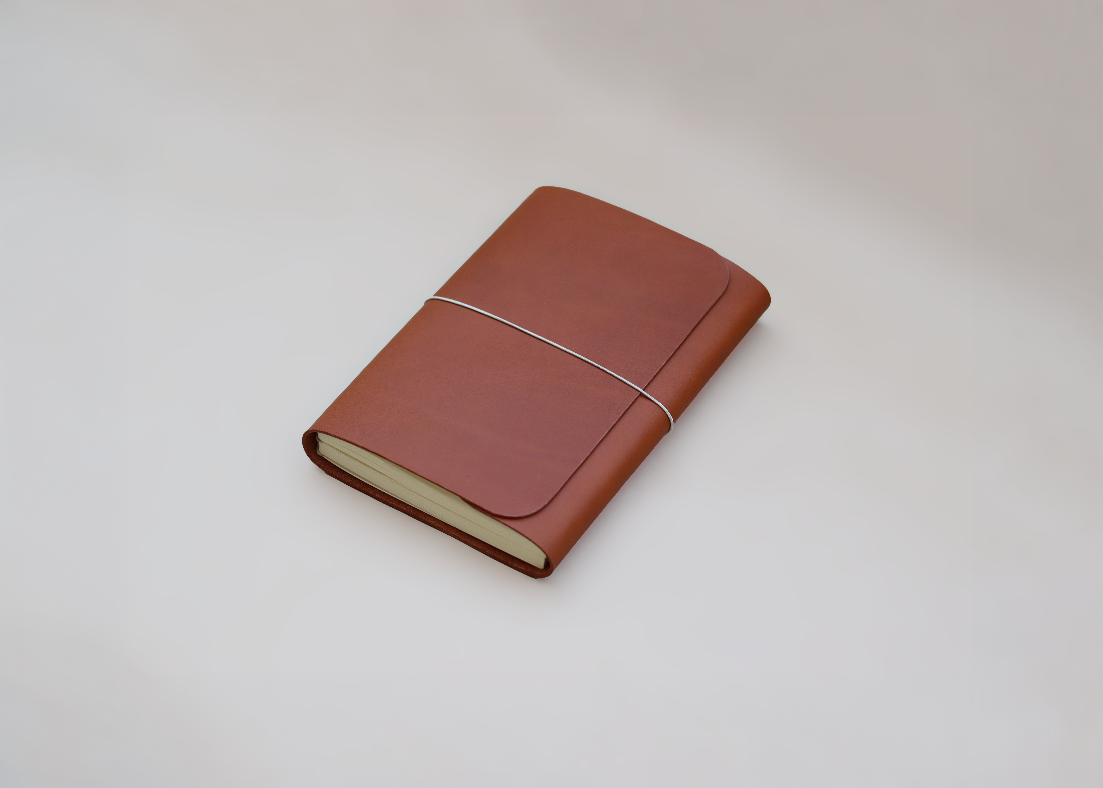 A brown leather journal with a curved cover, secured with a thin elastic band, resting on a light gray background.