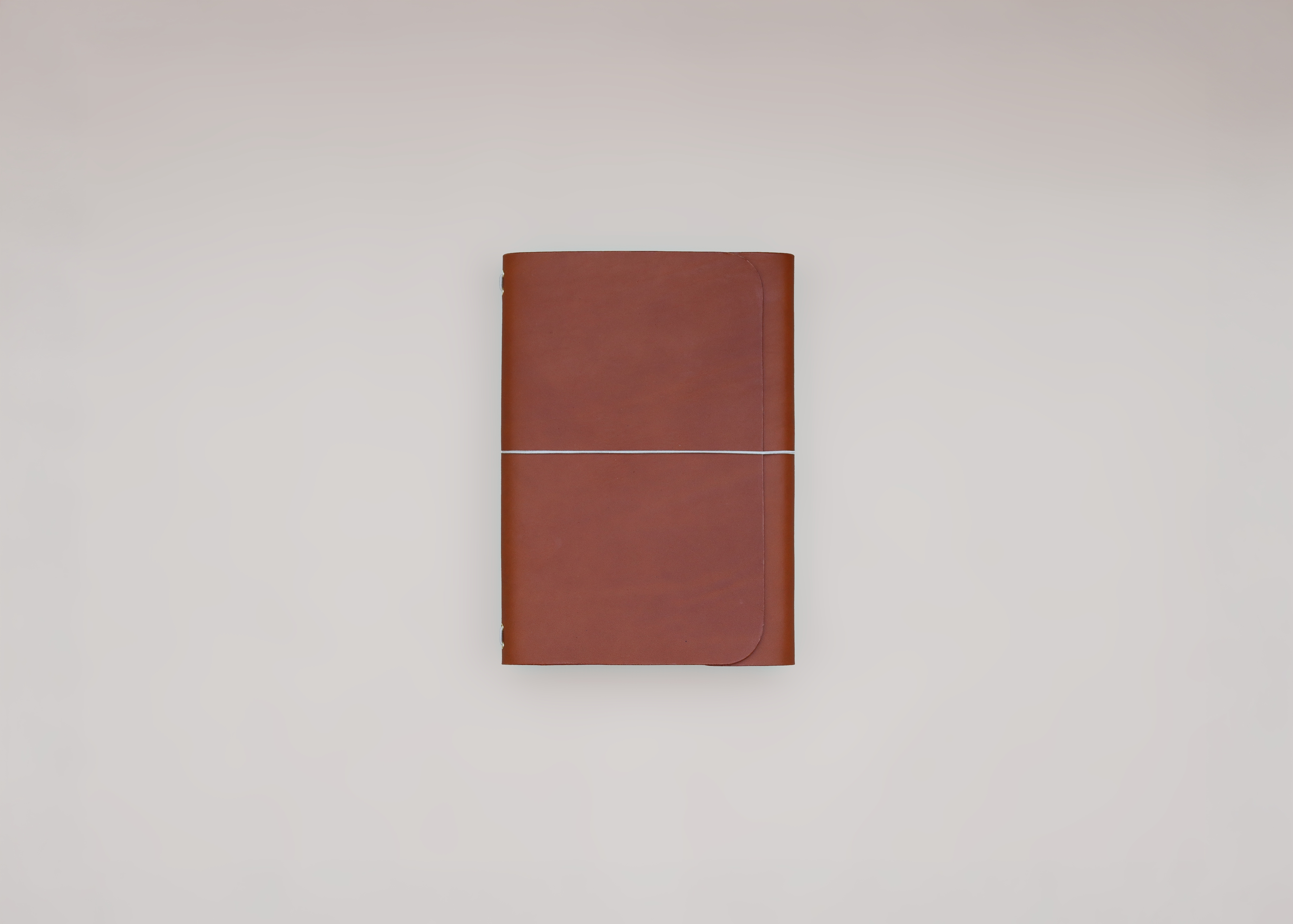 A brown leather journal with a light elastic across the front, shown closed against a neutral light gray background.