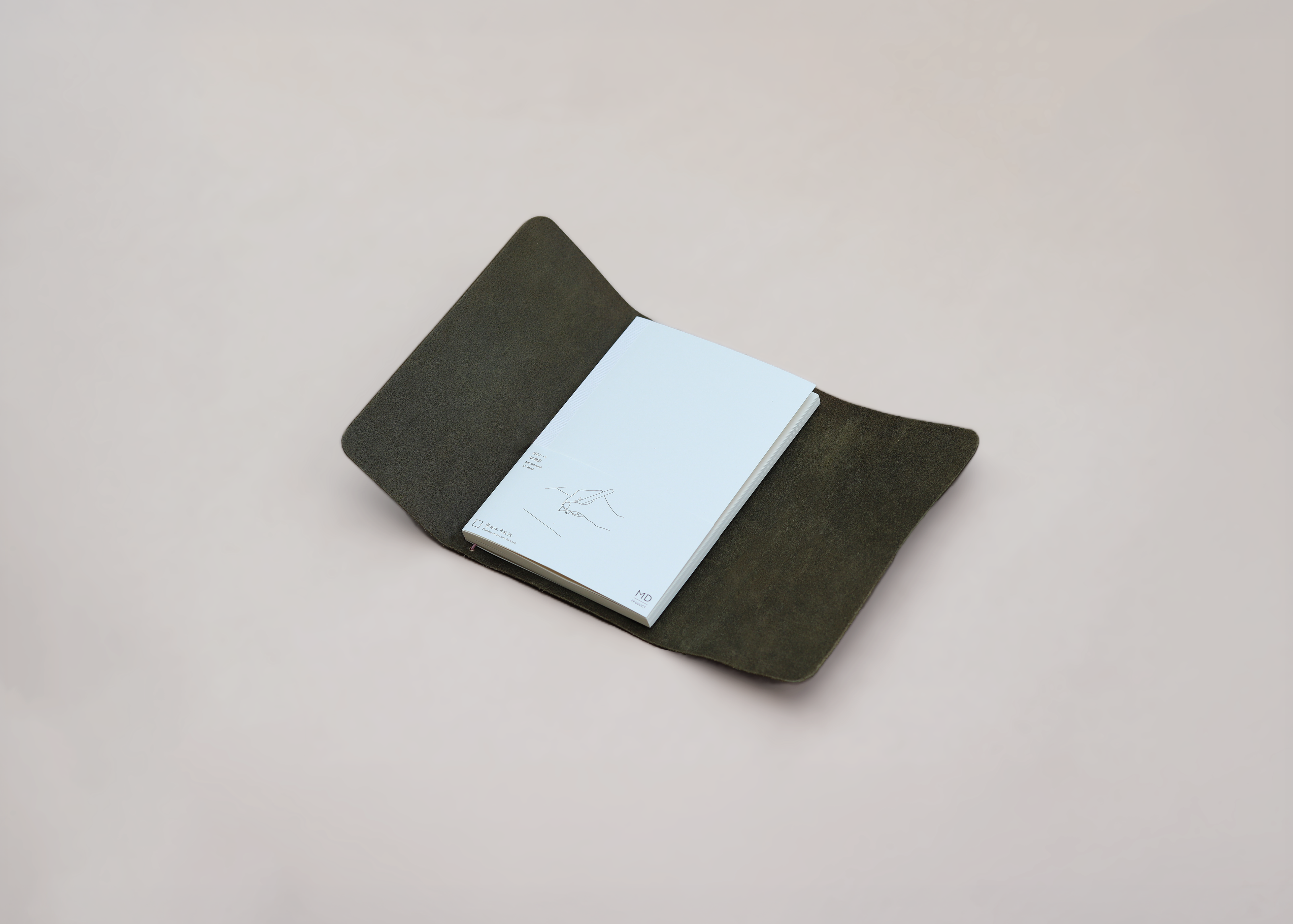 A dark olive green leather notebook cover holding a white notebook, photographed on a neutral light beige background.
