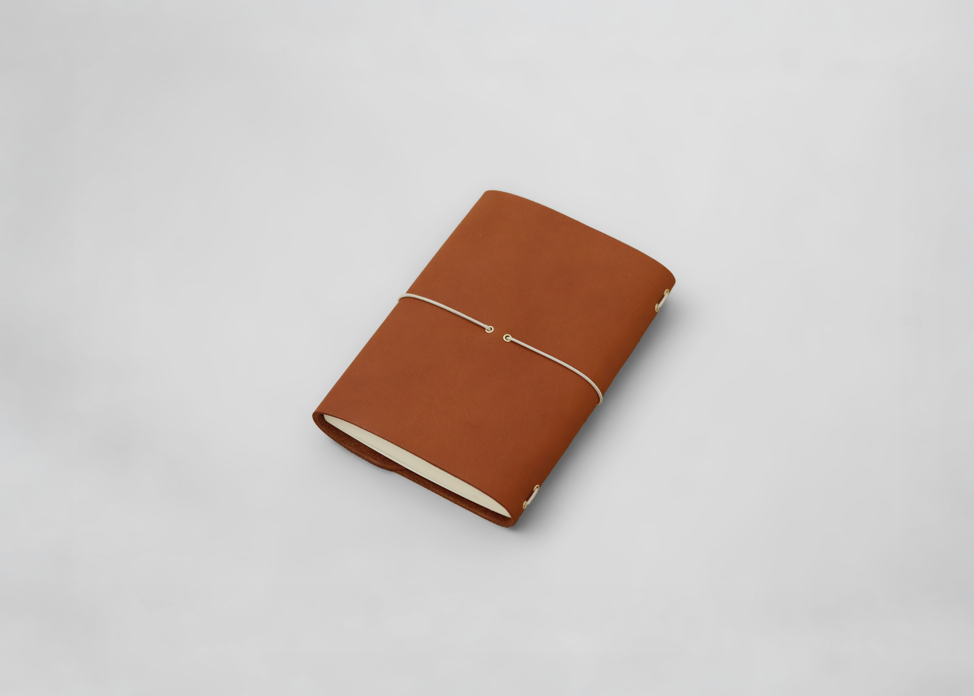 A brown leather journal with a thin elastic band closure, photographed on a clean light grey background.