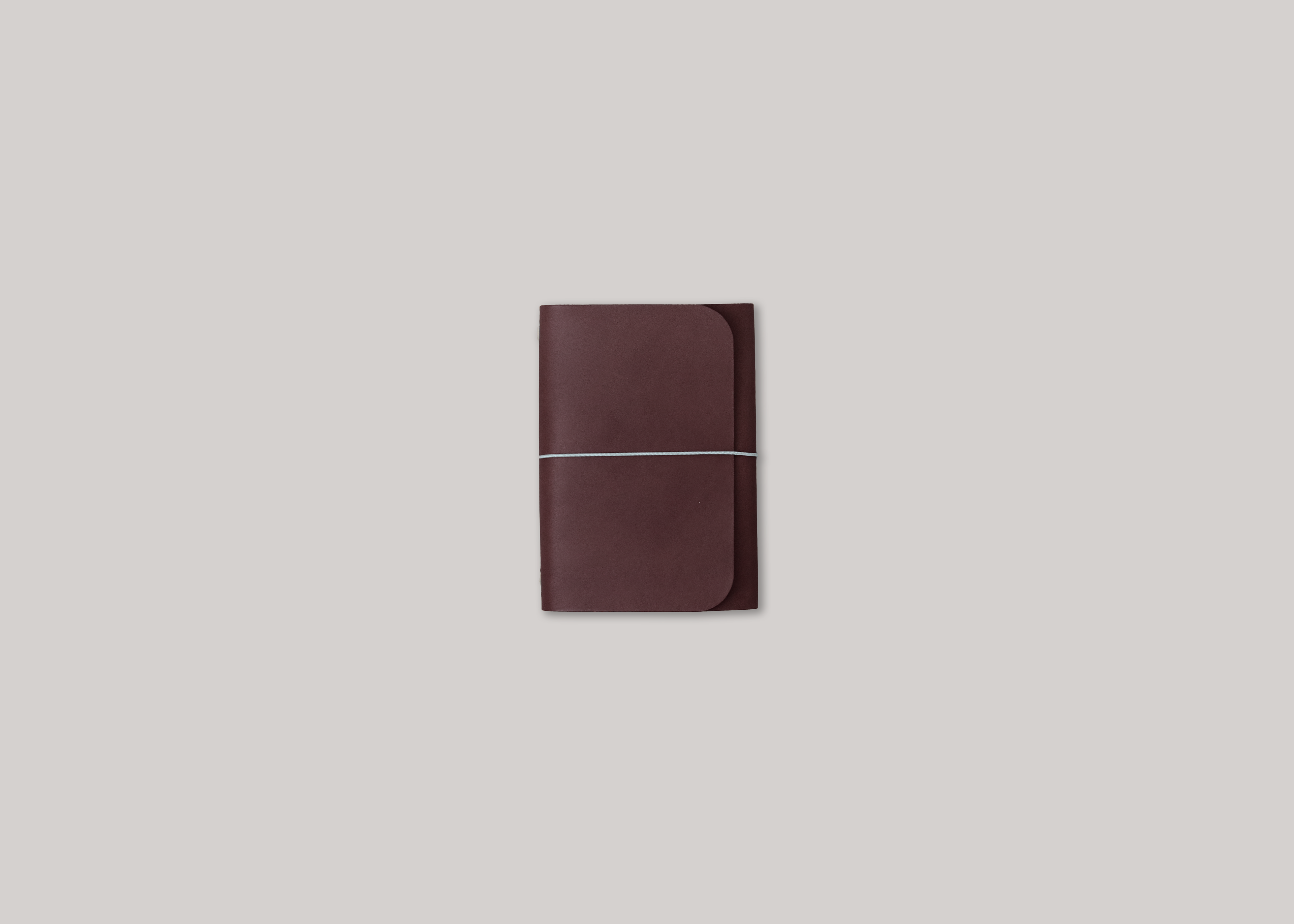 A dark brown leather journal with a horizontal elastic band closure, centered on a solid light grey background.