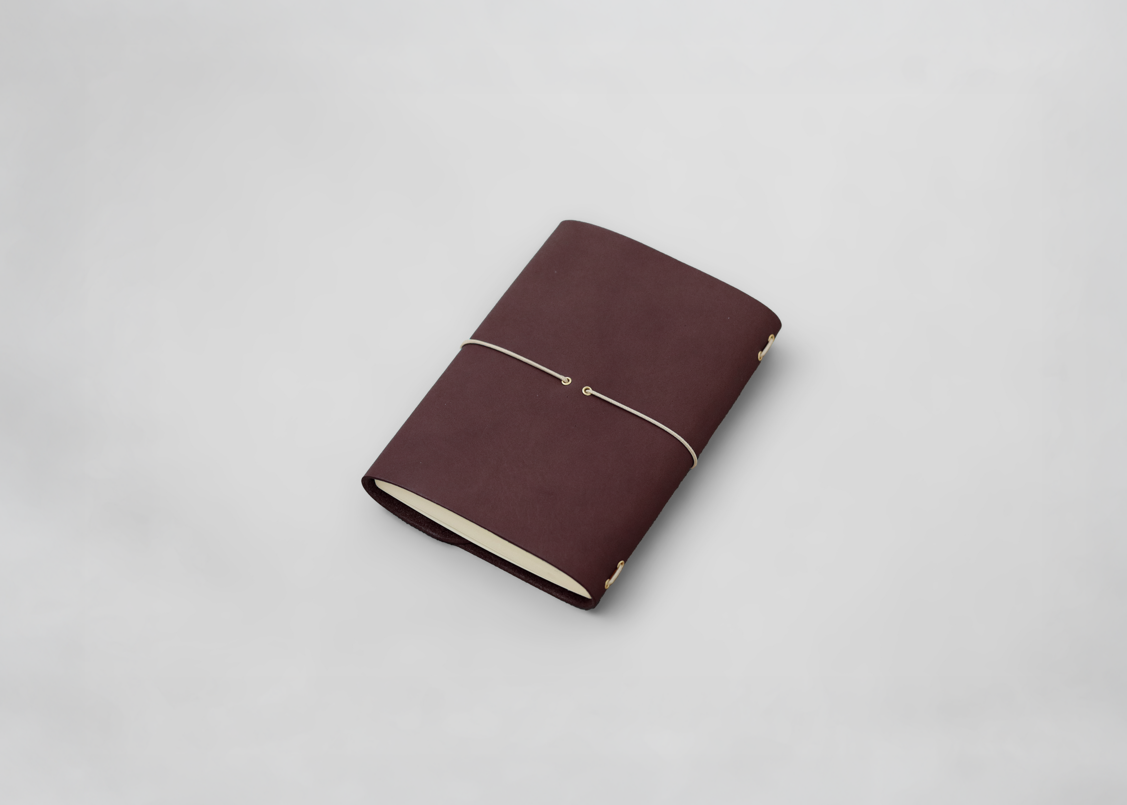 A dark burgundy leather journal with a thin ecru elastic band closure, resting on a light grey background.