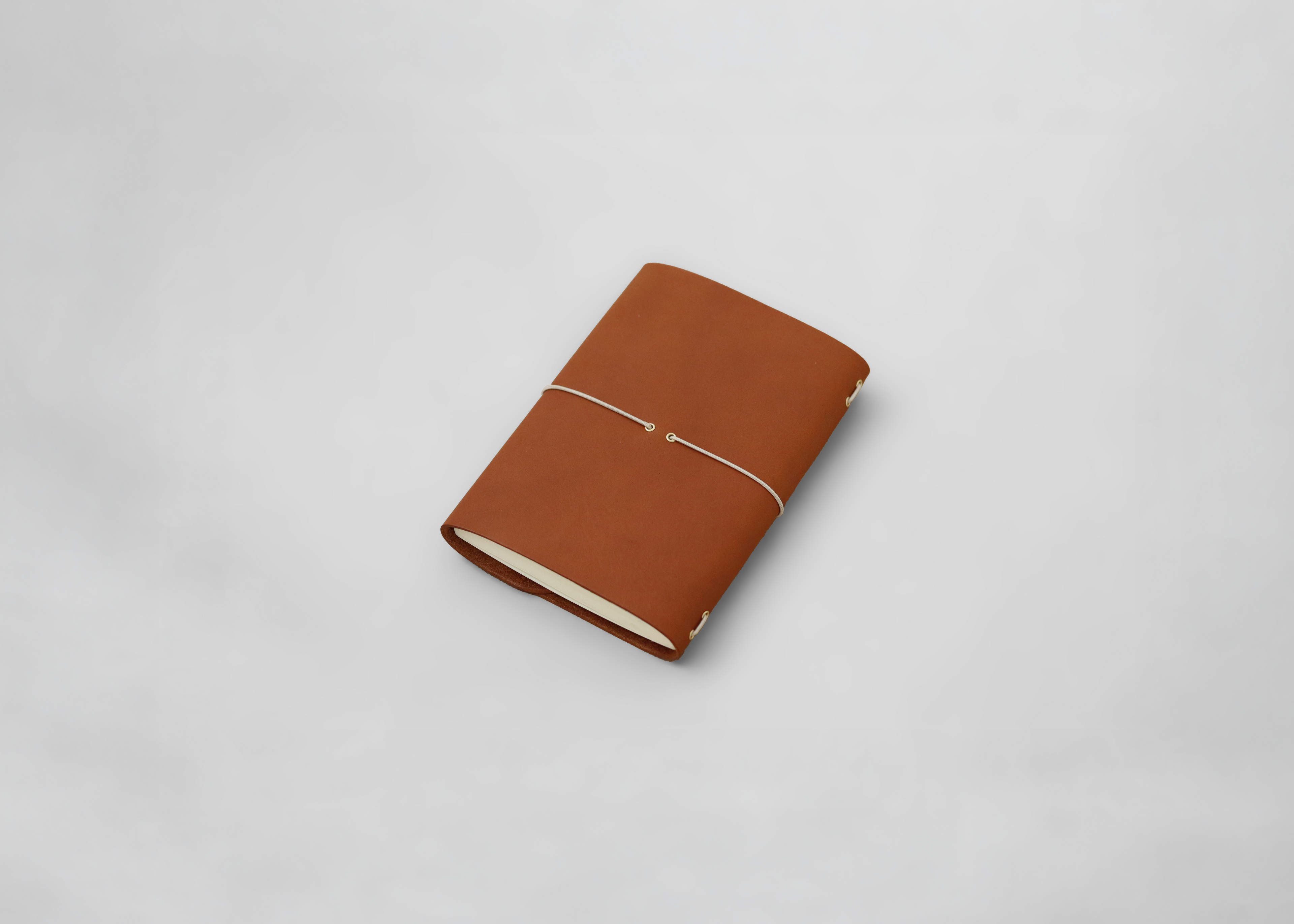 A brown leather journal with a thin elastic band closure, shown closed on a light gray background.
