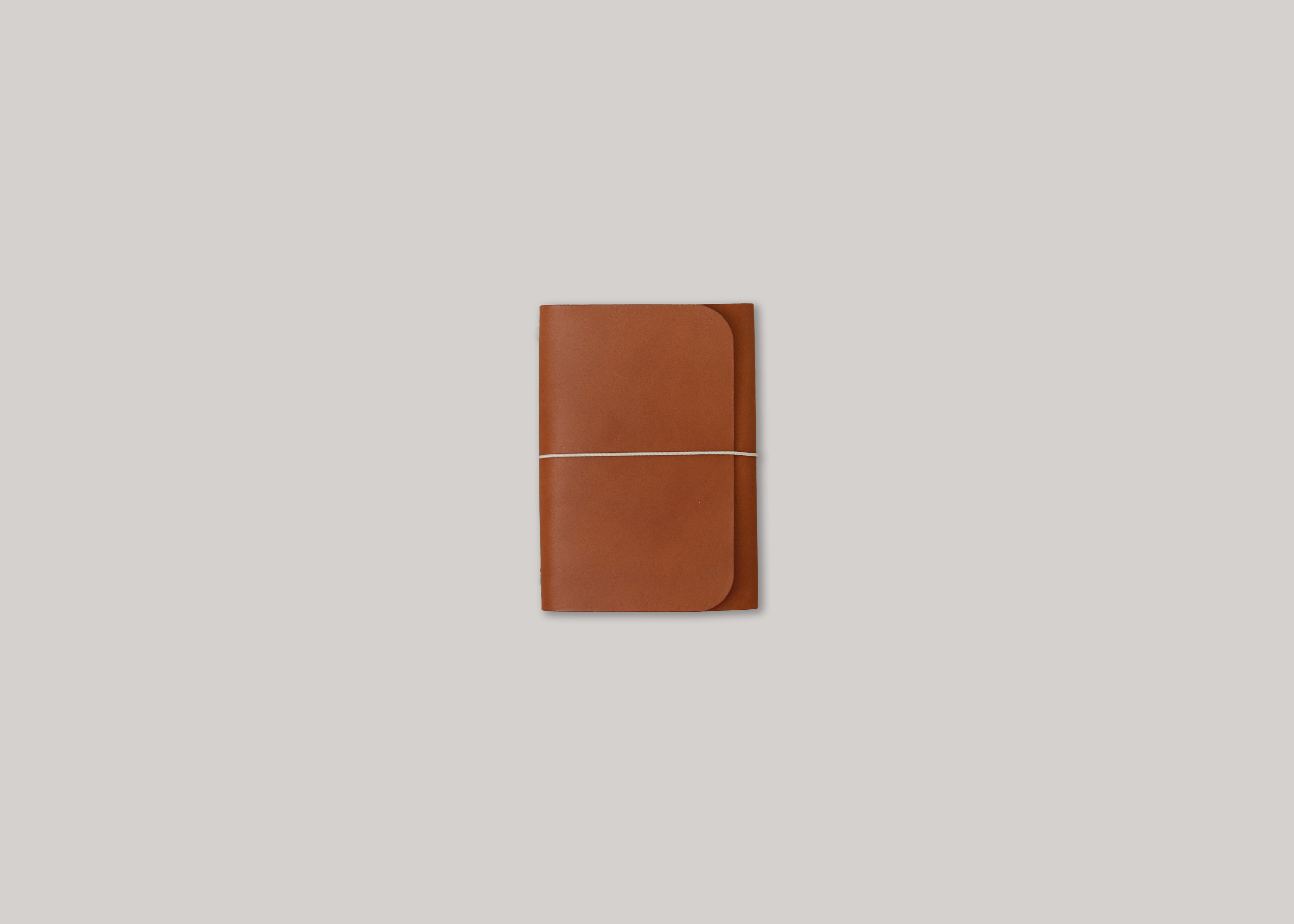 A brown leather notebook cover with a thin elastic closure, centred on a light grey background.