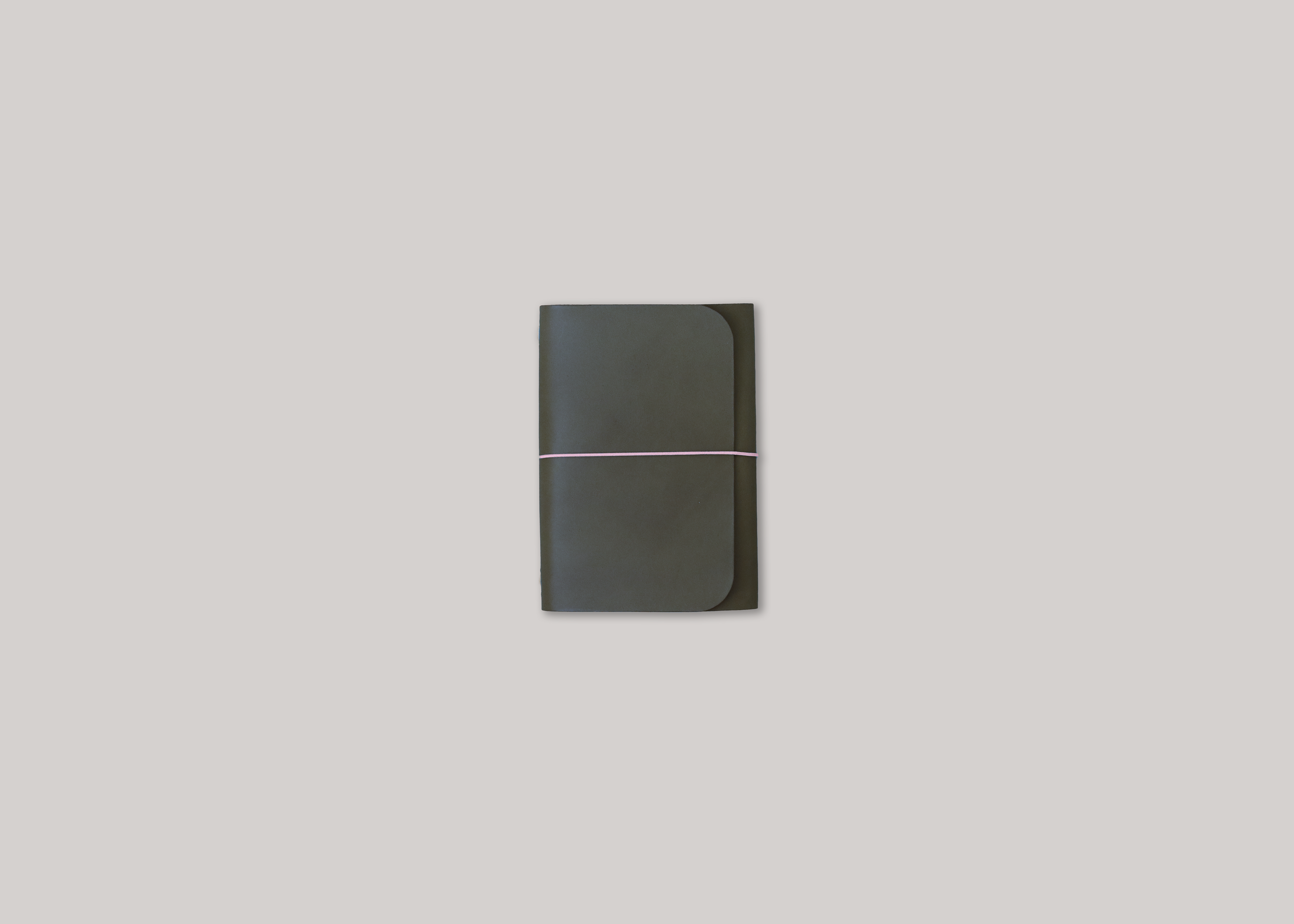 An olive green leather journal with a thin pink elastic band across the centre, shown against a solid light grey background.