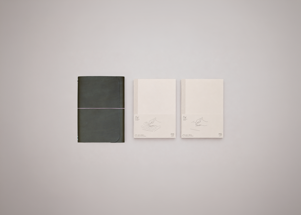 Olive green leather journal next to two white notebooks on a light grey background