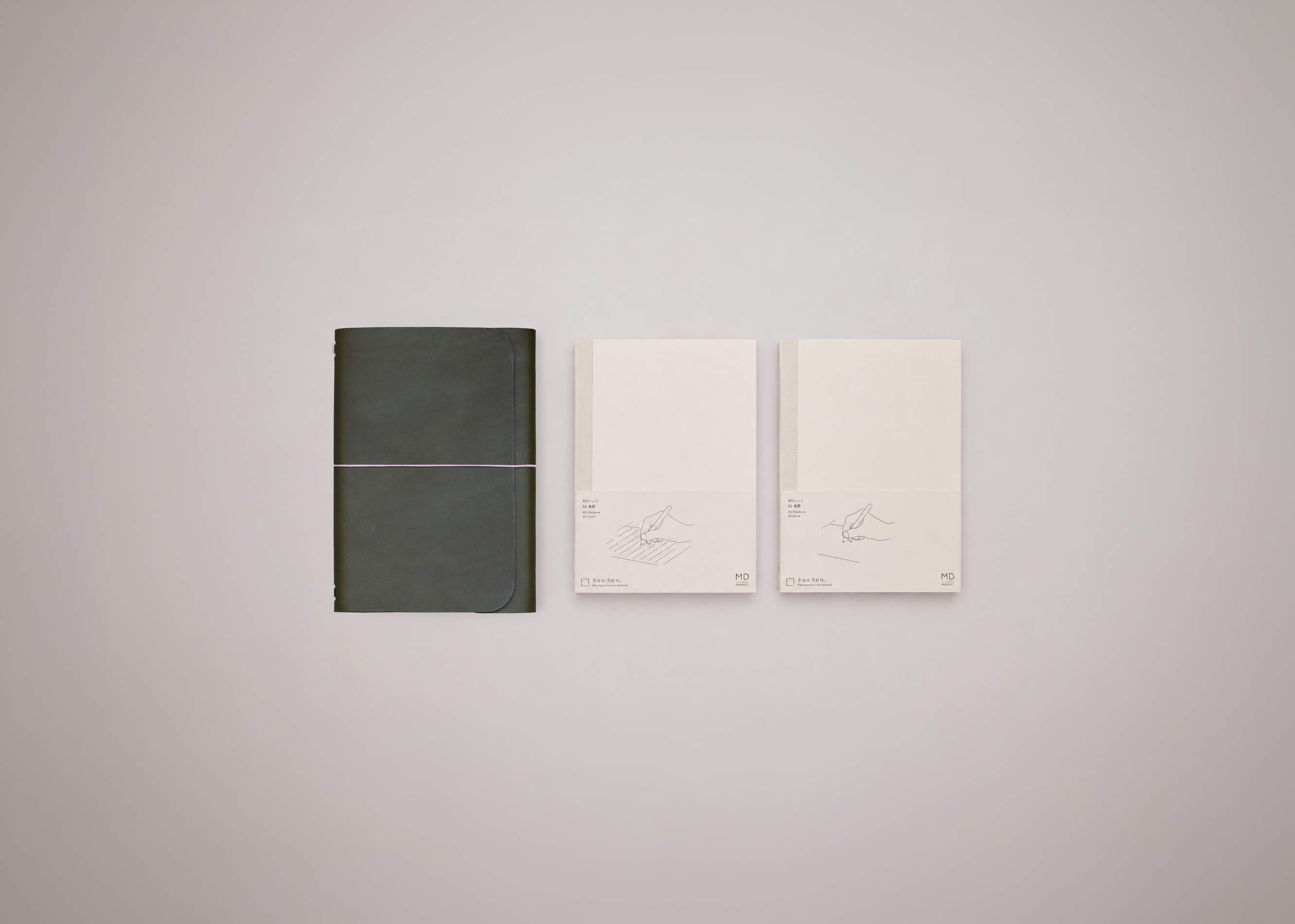 Olive green leather journal next to two white notebooks on a light grey background