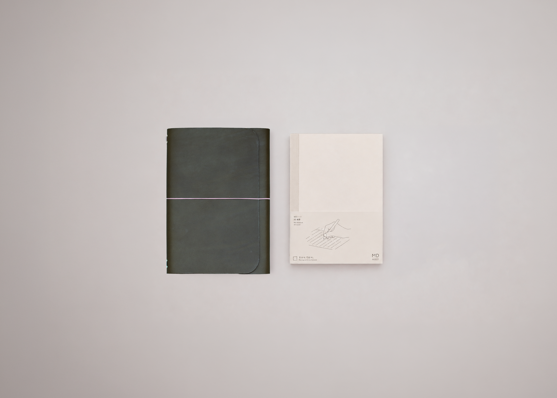 A minimalist olive green leather journal displayed next to a white notebook against a light grey background. 